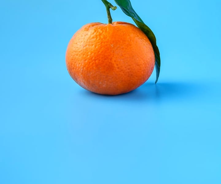 Orange with a still attached leaf on a light sky blue background